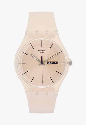 Montre Swatch beige avec index noirs, aiguilles argentées, trotteuse centrale violette et affichage jour-date indiquant lundi 1er.