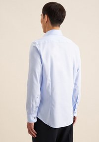 Camicia azzurro chiaro a maniche lunghe realizzata in tessuto liscio, con colletto a punta, polsini abbottonati e orlo curvo sul retro.