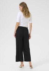 Pantalons larges noirs avec une taille élastique, fabriqués dans un tissu doux, associés à un haut blanc ajusté et des talons de couleur claire.