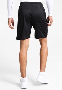 Czarne sportowe krótkie spodenki z elastycznym paskiem w talii, lekkiego materiału i gładkiej tekstury, noszone z białymi butami sportowymi.