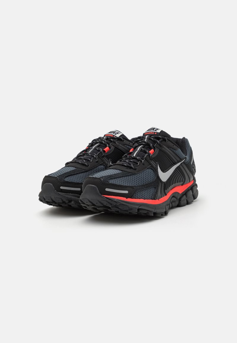 Baskets de sport noires et grises avec un dessus en mesh, des accents rouges, une semelle rembourrée et des détails réfléchissants sur les côtés et les lacets.