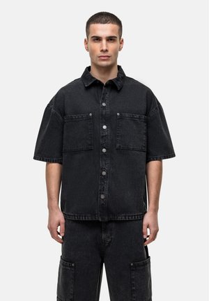 Camicia a maniche corte in denim nero con chiusura a bottoni, due tasche sul petto e vestibilità comoda, con una texture sottile e dettagli minimi.