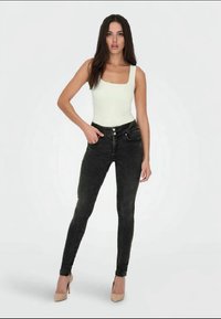 Czarne skinny jeansy z wysokim stanem, z pięcioma kieszeniami i metalowymi guzikami, w połączeniu z dopasowanym białym topem na ramiączkach.