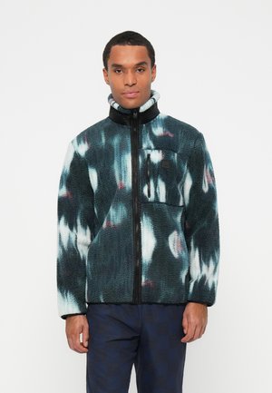 Fleece jacket in teal with abstract pink and white patterns. Features high collar, zip closure, and a left chest pocket with a black patch.