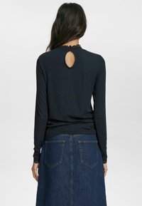 Svart långärmad topp med ett nyckelhålsöppning bak och spetsdetaljer vid halsringningen, ihop med en mörk denimkjol med bakfickor.