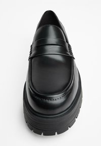 Zwarte leren loafer met een glad oppervlak en een licht verhoogde, getextureerde platformzool. Heeft een band over de bovenkant voor detail.