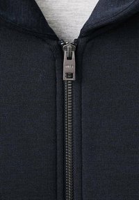 Chaqueta de hombre azul marino con cremallera, fabricada con un tejido texturizado, cremallera plateada y cuello alto. El interior es de un color gris claro y suave.