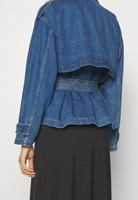 Jeansjacka i ljusblå med peplumdesign. Har bälte i midjan, långa ärmar och knappade ärmslut. Sitter ovanför midjan.