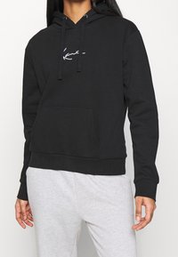Felpa nera con cappuccio realizzata in un morbido mix di cotone, presenta una tasca a marsupio, cordini regolabili e un logo bianco minimalista sul petto.