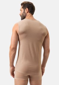 Débardeur sans manches couleur beige avec un tissu texturé, présenté sur une personne vue de dos. La coupe est ajustée, avec un ourlet inférieur court.