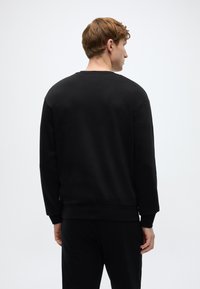 Μαύρο φούτερ με σ τρογγυλή λαιμόκοψη, μακριά μανίκια και ριμπ μανσέτες· κατασκευασμένο από απαλό ύφασμα, με απλό, καθαρό σχεδιασμό.