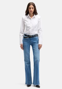 Biała koszula zapinana na guziki z długimi rękawami, w połączeniu z jasnoniebieskimi rozszerzanymi dżinsami i czarnym paskiem. Buty to czarne szpilki z węższym czubkiem.