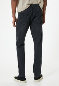 Jeans de mezclilla gris oscuro con un diseño de pierna recta, que presentan bolsillos traseros y un acabado limpio. El material parece resistente con un ligero desgaste.