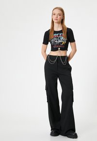 Sort cropped t-shirt med grafisk tryk og korte ærmer, parret med vide sorte cargobukser med sidelommer og sølv kæde detaljer.