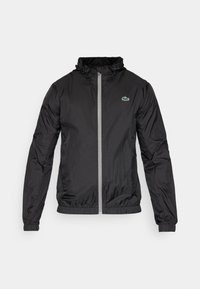 Zwarte lichtgewicht jas, gemaakt van ripstopstof, met een rits aan de voorkant, een trekkoord capuchon, elastische manchetten en een klein groen logo op de borst.