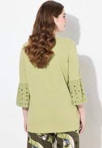 Top verde chiaro, dall'aspetto morbido e con maniche a 3/4, che presenta ricami a intaglio. Tessuto soffice, design casual, abbinato a pantaloni con motivo.