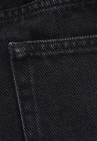 Close-up of black denim fabric showing detailed stitching and the edge of a back pocket.