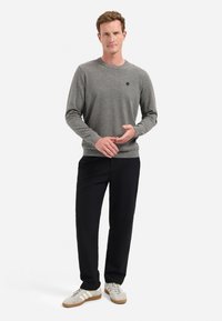 Grijze trui met een ronde hals, minimale uitstraling en klein logo; gecombineerd met zwarte broek en witte sneakers met beige accenten.