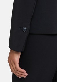 Černý přiléhavý blazer s hladkou texturou, precizním šitím a detaily na manžetách s knoflíkem. Design je navržen pro moderní střih.