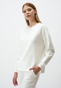 Felpa bianca in cotone misto con scollatura a girocollo, vestibilità rilassata e spalle scese. La trama appare liscia. Abbinata a pantaloni coordinati.