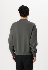 Gray sweatshirt with a crew neck, drop shoulders, and ribbed cuffs. Soft fabric texture; no visible graphics or patterns.