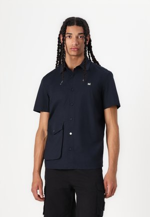 Short-sleeve, dark navy shirt with a button front, patch pocket, and subtle logo. Smooth fabric and structured collar detail.