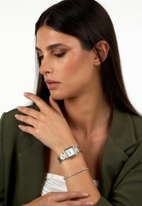 Orologio da polso in tonalità argento e oro con cassa rettangolare, quadrante bianco e cinturino in acciaio inossidabile. Accompagnato da un delicato braccialetto argento.