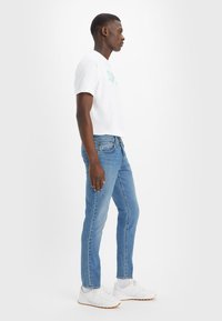 Slim fit modre jeans z klasičnim petimi žepi, v kombinaciji z belo majico s kratkimi rokavi in belimi supergami.
