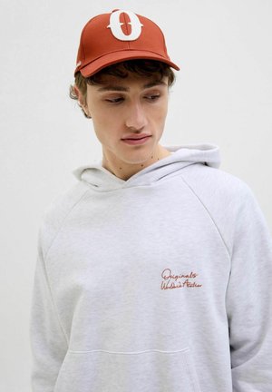 Red cap with a large white "O" logo, paired with a light gray hoodie featuring a textured, embroidered brand name on the chest.