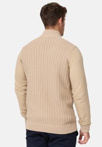 Suéter de punto beige con un respaldo texturizado, mangas suaves, cuello alto y dobladillo acanalado. El diseño presenta un punto con patrón.