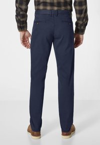 Marineblaue Hose mit glatter Stoffoberfläche, ausgestattet mit Gesäßtaschen und geradem Schnitt, kombiniert mit braunen Schuhen.