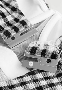 Bh-strop med et vævet teksturmønster i sort, grå og hvid. Metalclips er fastgjort til en mesh-stof baggrund. Blød hvid foring synlig.