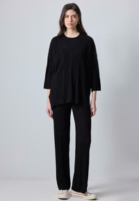 Black knitted two-piece outfit featuring a loose-fitting, V-neck top with elbow-length sleeves and matching wide-leg pants with ribbed texture.