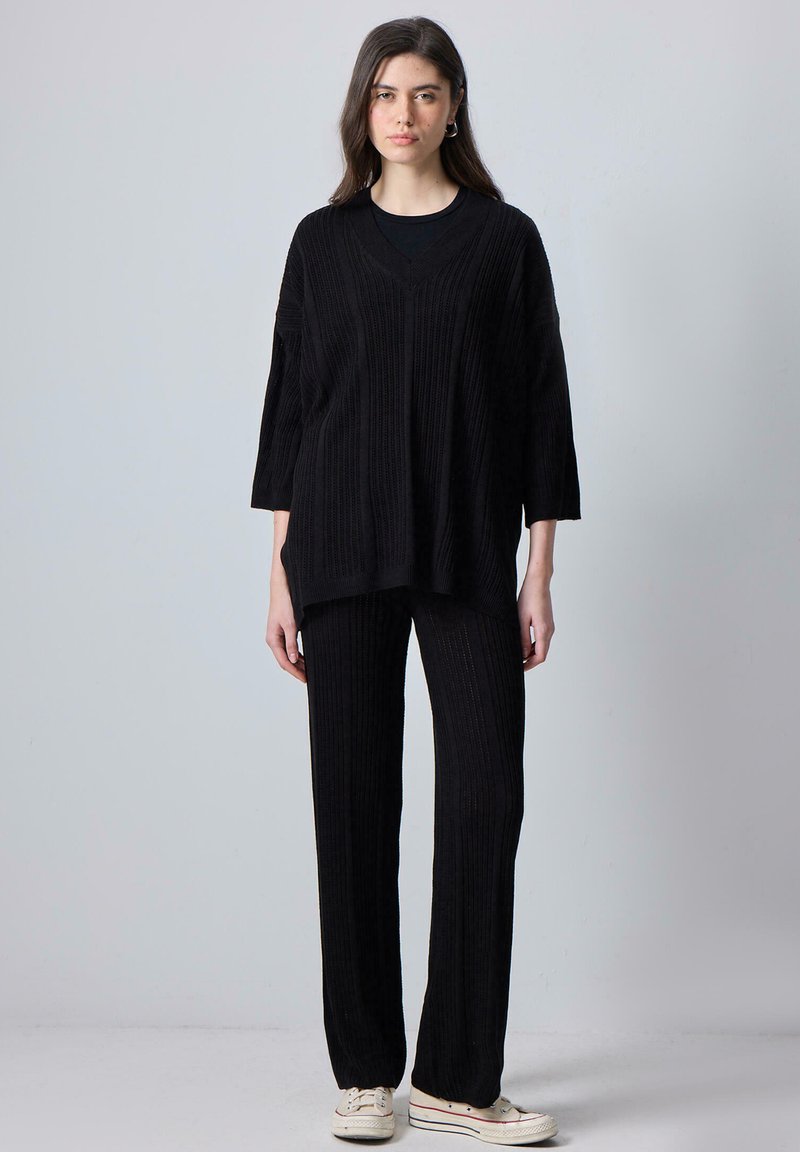 Black knitted two-piece outfit featuring a loose-fitting, V-neck top with elbow-length sleeves and matching wide-leg pants with ribbed texture.