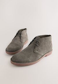 Graue Wildleder-Stiefeletten mit abgerundeter Spitze, minimalistischem Design und kontrastierender Gummisohle. Verfügt über zwei Ösen und dezente Nahtakzente.
