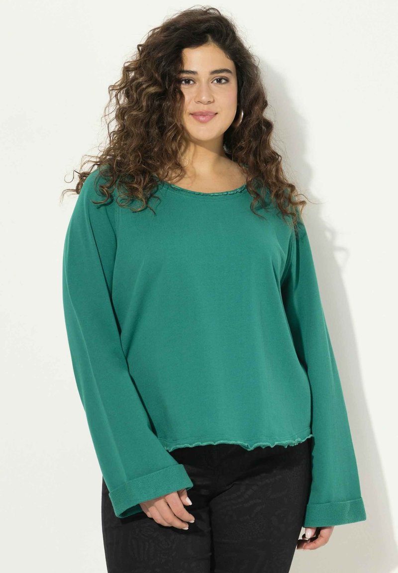Maglia verde a maniche lunghe con colletto rotondo a coste, vestibilità comoda e orlo grezzo. Il materiale sembra morbido, con maniche ampie e dettagli di cucitura minimi.