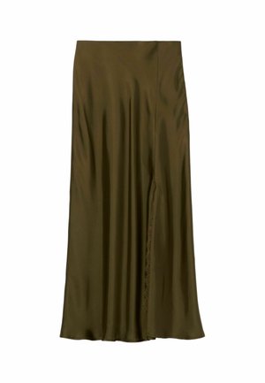 Donna con blusa bianca a maniche corte e gonna midi verde oliva, che tiene una piccola borsa marrone, in piedi davanti a uno sfondo grigio uniforme.