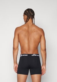 Schwarze Boxershorts mit einer figurbetonten Passform, ausgestattet mit einem weißen Logo-Bund an der Taille. Der Stoff wirkt glatt und dehnbar.