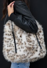 Torebka z sztucznego futra w beżowo-białe cętki, z czarnymi skórzanymi akcentami i detalami zamka błyskawicznego. Miękka w dotyku i przestronna.