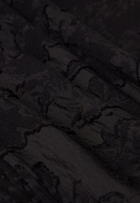 Zwart textiel met een subtiel patroon, met gelaagde plooien die diepte creëren. Het materiaal lijkt zacht en licht gekreukt.