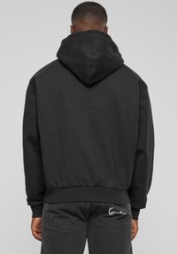 Sudadera negra con una capucha grande, puños y dobladillo acanalados y tejido suave. Presenta un logo bordado en blanco en la parte posterior cerca de la cinturilla.
