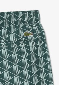 Groen stoffen patroon met een geometrisch wit design, elastische tailleband en geborduurd groen krokodillenlogo.