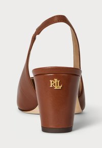 Hnedé kožené sandále na vysokom podpätku s okrúhlou špičkou a remienkom. Má zlato kovový logotyp na podpätku a textúrovaný povrch.