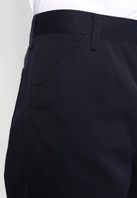 Marineblauwe broek gemaakt van duurzame stof, met een gladde textuur en een rechte snit, voorzien van contrasterende stiksels en een zijzak.