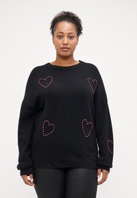 Črn oversize sweatshirt iz teksturiranega pletenega materiala, ki ima kot okras rdeče srčne žebljičke, ter rebrast ovratnik in rob.
