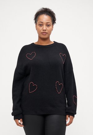 Black oversized sweatshirt made of a textured knit, featuring red heart-shaped studs as accents, with a ribbed neckline and hem.
