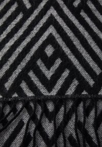 Écharpe noire et grise à motif géométrique, bords à franges, texture douce et motifs en chevron bien visibles.