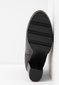 Semelle de chaussure en cuir noir avec talon, présentant trois rainures horizontales dans la zone des orteils sur un fond blanc.