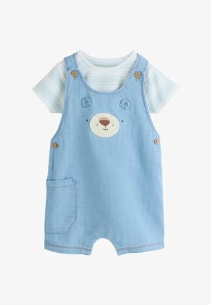 Šviesiai mėlynas kūdikio kombinezonas su meškutės veido dizainu, su sagomis ant petnešėlių, šonine kišene, dėvimas ant balto trumpomis rankovėmis marškinėlių su šviesiai žaliomis juostelėmis.