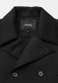 Zwarte double-breasted jas kraag met twee zichtbare knopen en een zwart label aan de binnenkant met de tekst "someday." in witte letters.